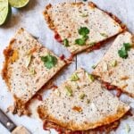 Spicy tuna quesadillas cut into wedges on a white wooden board, filled with tuna, red pepper and melted cheese, garnished with spring onion and coriander, with a knife and halved limes alongside